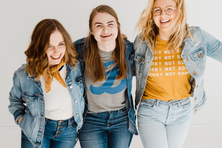 Studio shot of three girlfriends on white background laughing with their arms around each other