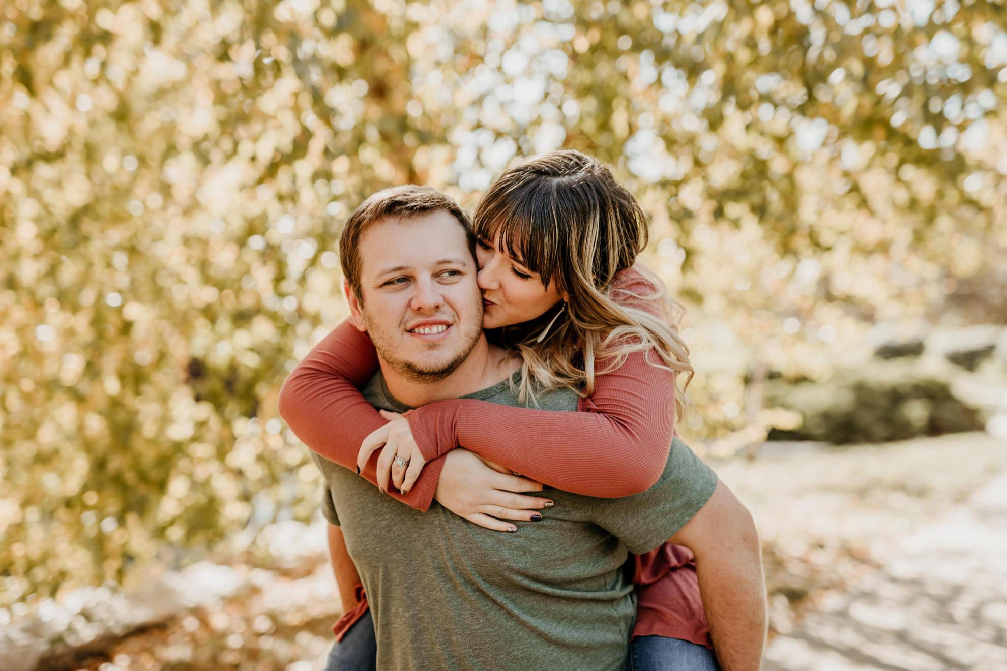 husband giving wife piggy back ride in park during fall