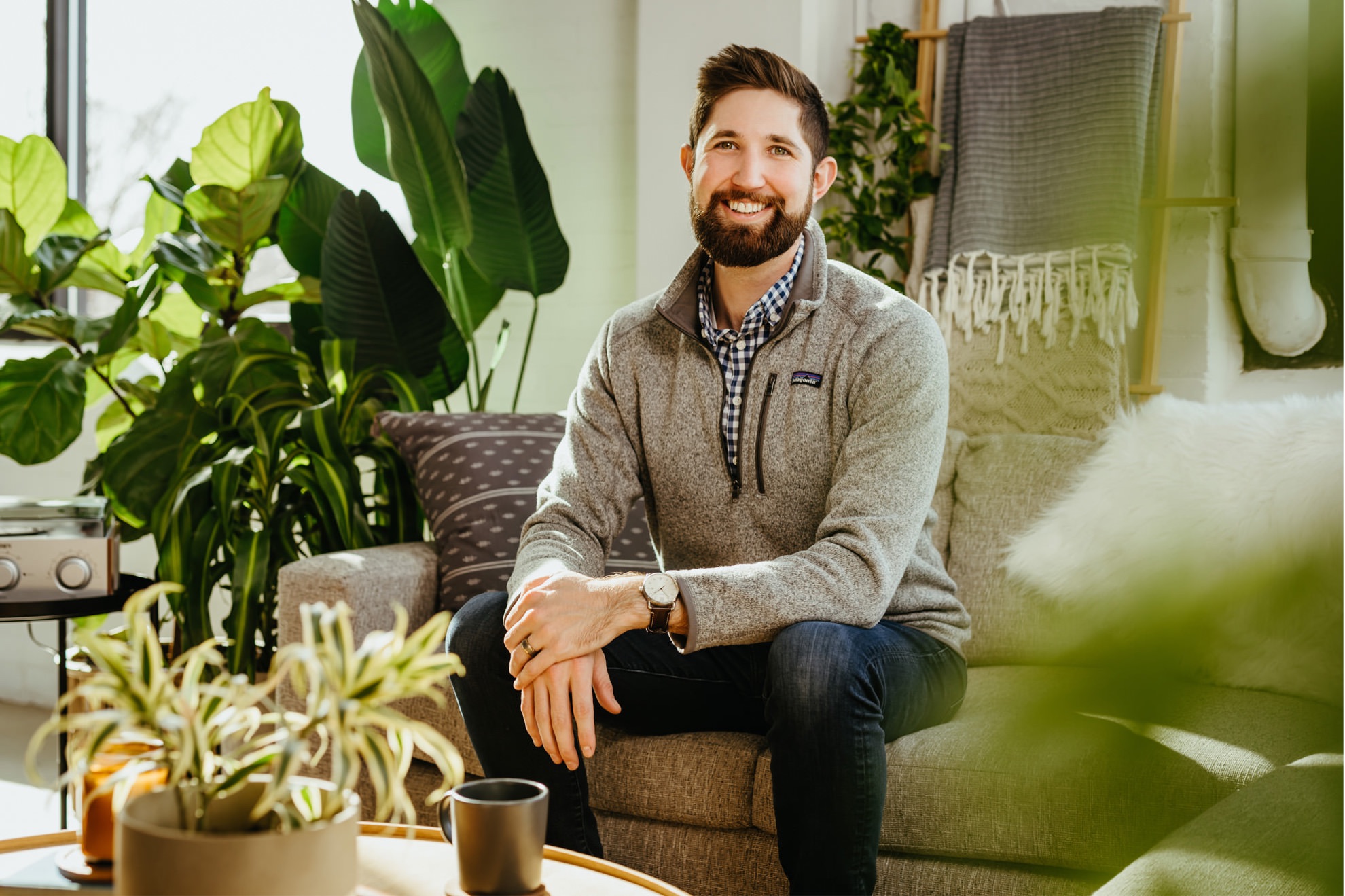 cozy portrait of man sitting on couch smiling surrounded by green plants