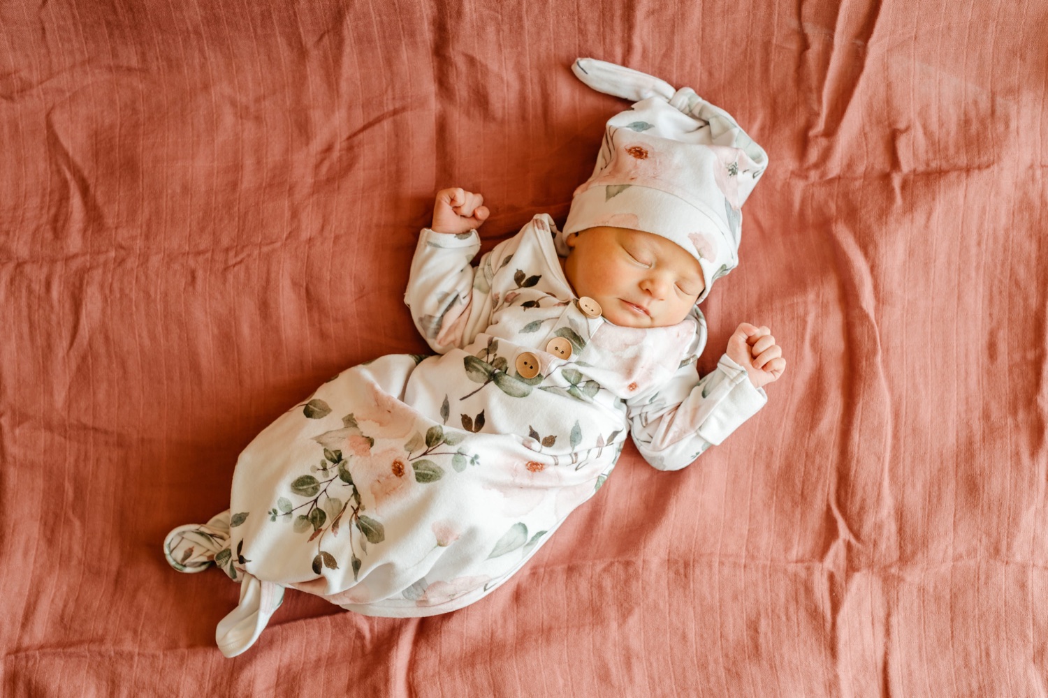 newborn baby girl in floral swaddle laying on pink blanket